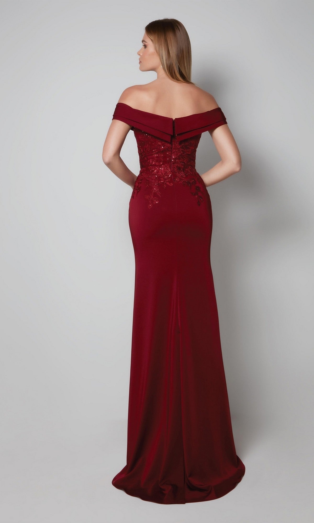 A woman faces away from the camera, modeling the Alyce 27571 long formal dress—a dark red, off-the-shoulder gown in stretch-crepe with floor-length hem and lace-detailed bodice.